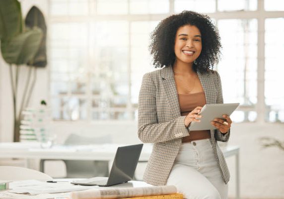 Happy businesswoman using a digital tablet. Young leading businesswoman using a wireless tablet. Creative designer working in her agency. Designer standing in her office using an online app