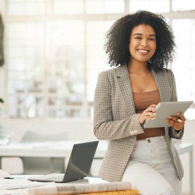 Happy businesswoman using a digital tablet. Young leading businesswoman using a wireless tablet. Creative designer working in her agency. Designer standing in her office using an online app